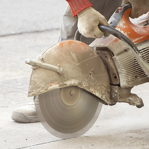 A male construction worker saws asphalt with a seam cutter, dust swirls from under the saw, construction and road work to repair the coating.