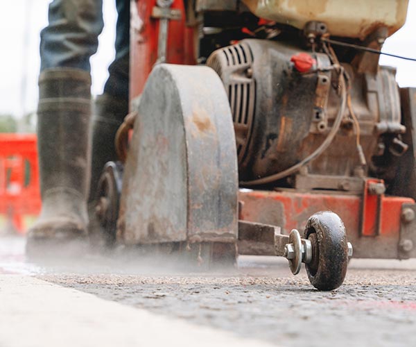 Construction worker cutting asphalt road surface with petrol power road saw and diamond blade during roadworks