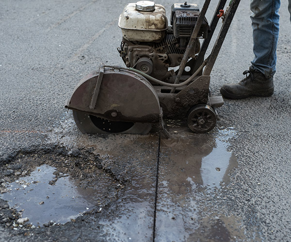 Worker cuts a piece of asphalt using a cutting machine pavement. The machine for cutting asphalt. Pothole on the road.Worker cuts piece of asphalt using a cutting machine pavement. The machine for cutting asphalt. Pothole on the road.
