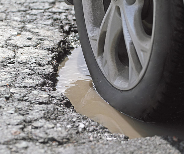 Closeup shot of a vehicle slowly driving through a pothole, demonstrating the possible damage to tire and wheel. Shallow dof with focus on image centre.